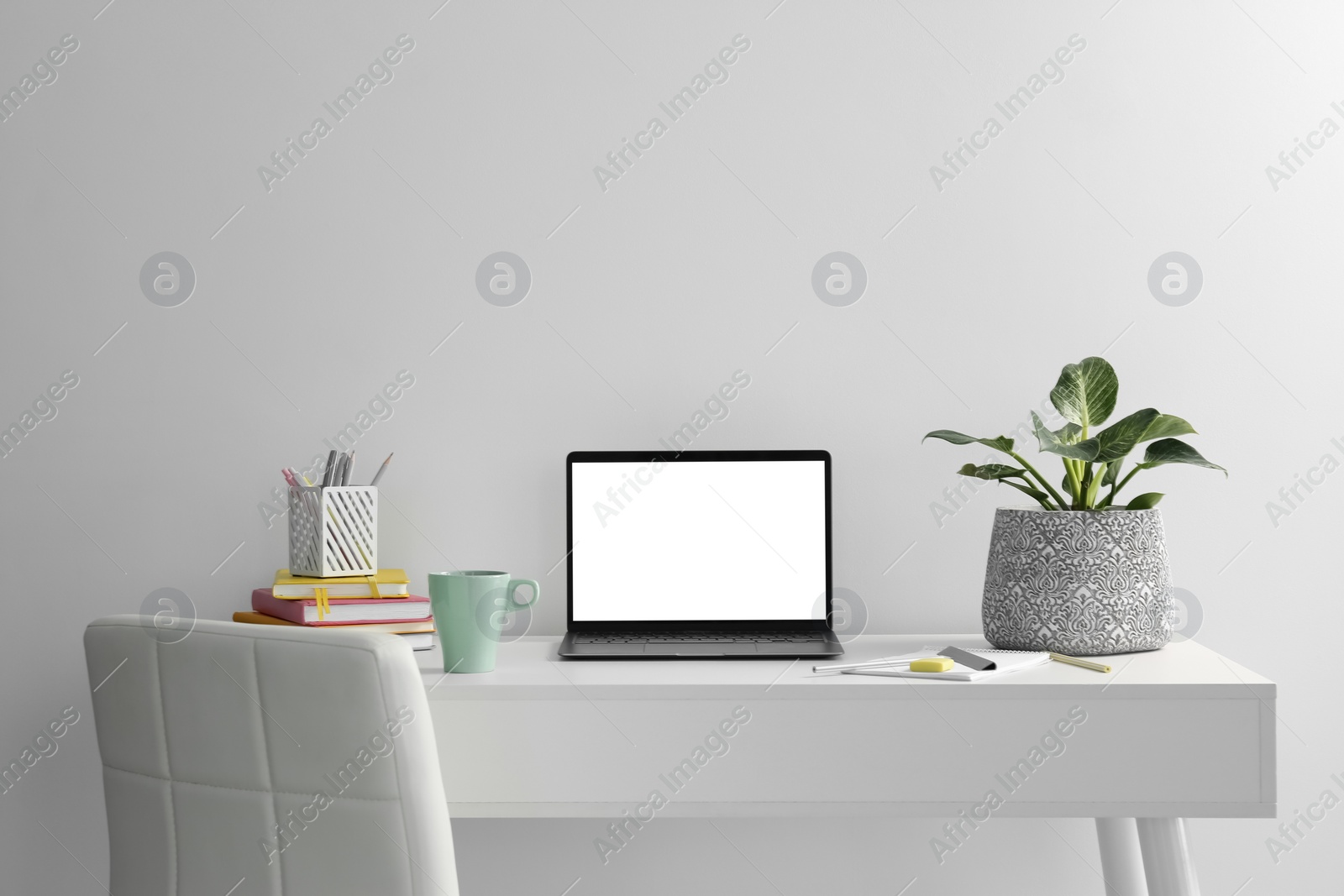 Photo of Stylish workplace with laptop, houseplant, stationary and cup on table near white wall