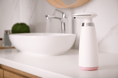 Modern automatic soap dispenser on countertop in bathroom. Space for text