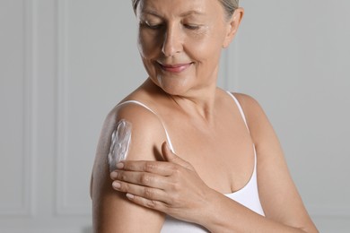 Photo of Happy woman applying body cream on shoulder near white wall