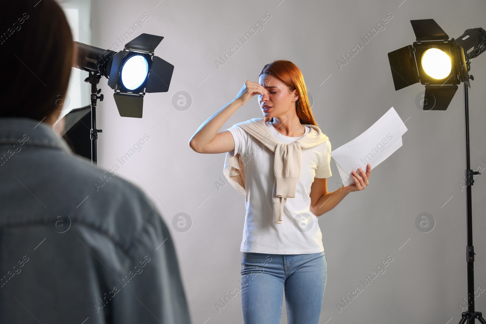 Photo of Emotional woman with script performing in front of casting director against grey background at studio