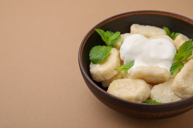 Bowl of tasty lazy dumplings with sour cream and mint leaves on light brown background. Space for text
