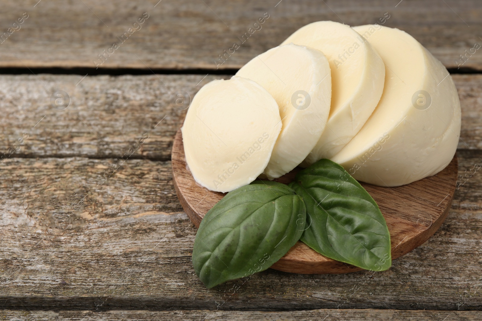 Photo of Board with tasty mozzarella slices and basil leaves on wooden table, closeup. Space for text