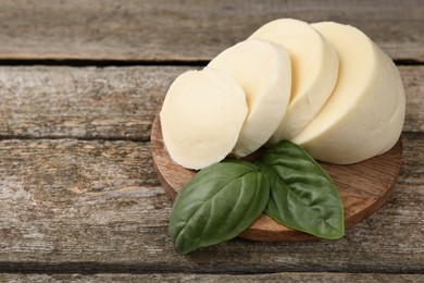 Photo of Board with tasty mozzarella slices and basil leaves on wooden table, closeup. Space for text