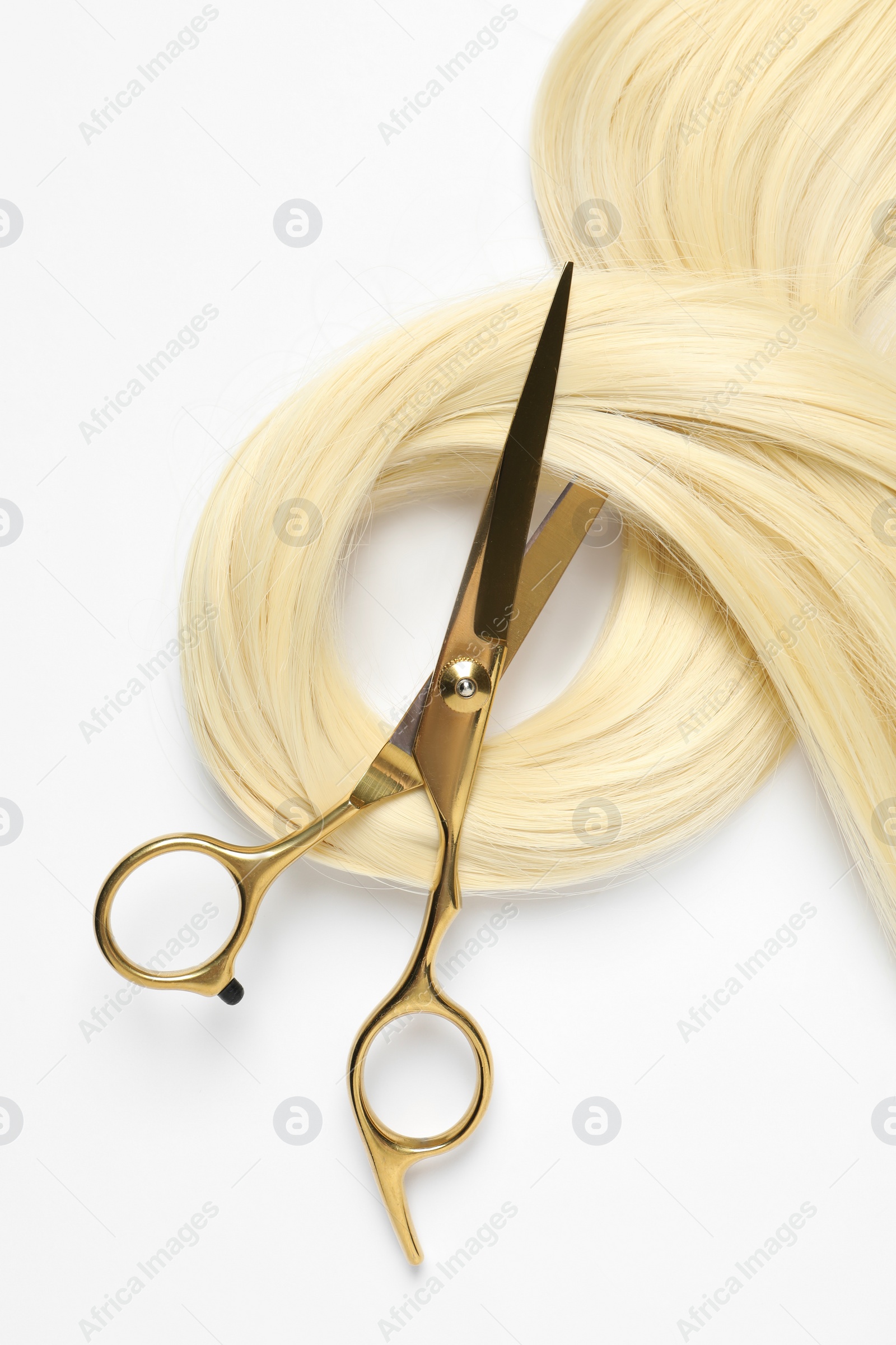 Photo of Professional hairdresser scissors with blonde hair strand on white background, top view