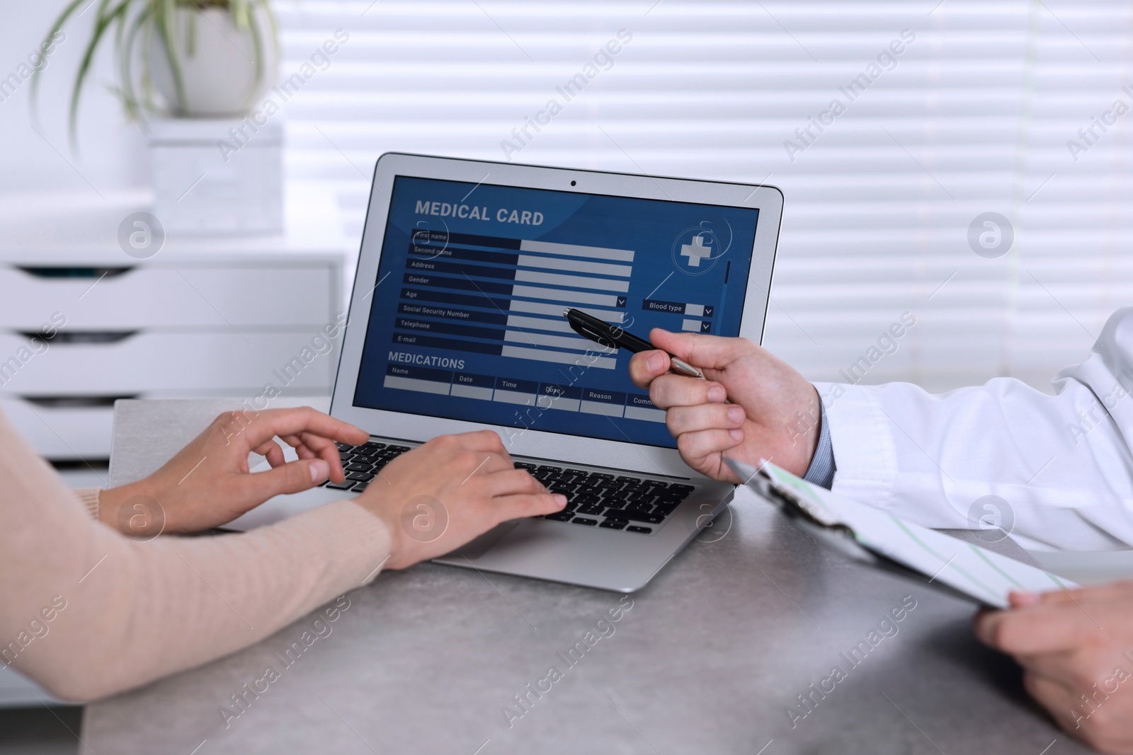 Photo of Doctor and patient using laptop to fill out medical card at table in clinic, closeup