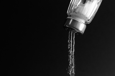 Photo of Pouring salt from shaker on black background, closeup. Space for text