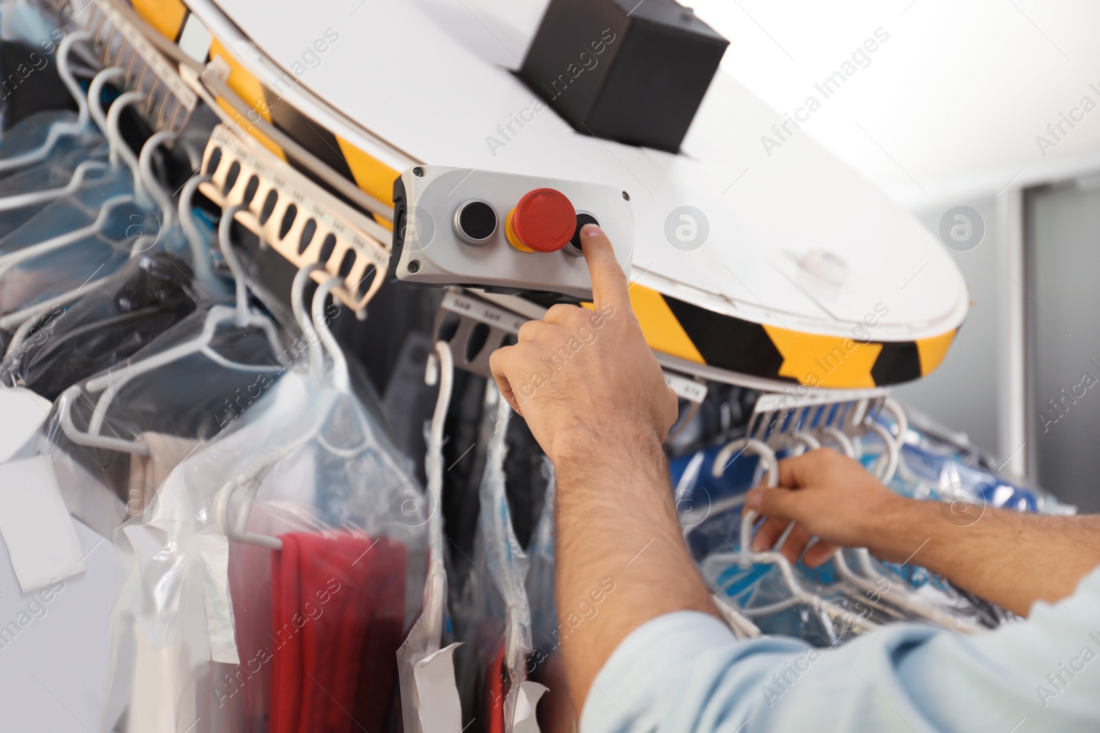 Photo of Worker pressing button on control panel of garment conveyor at modern dry-cleaner's, closeup