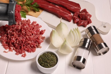 Photo of Manual meat grinder with beef, onion and spices on white wooden table