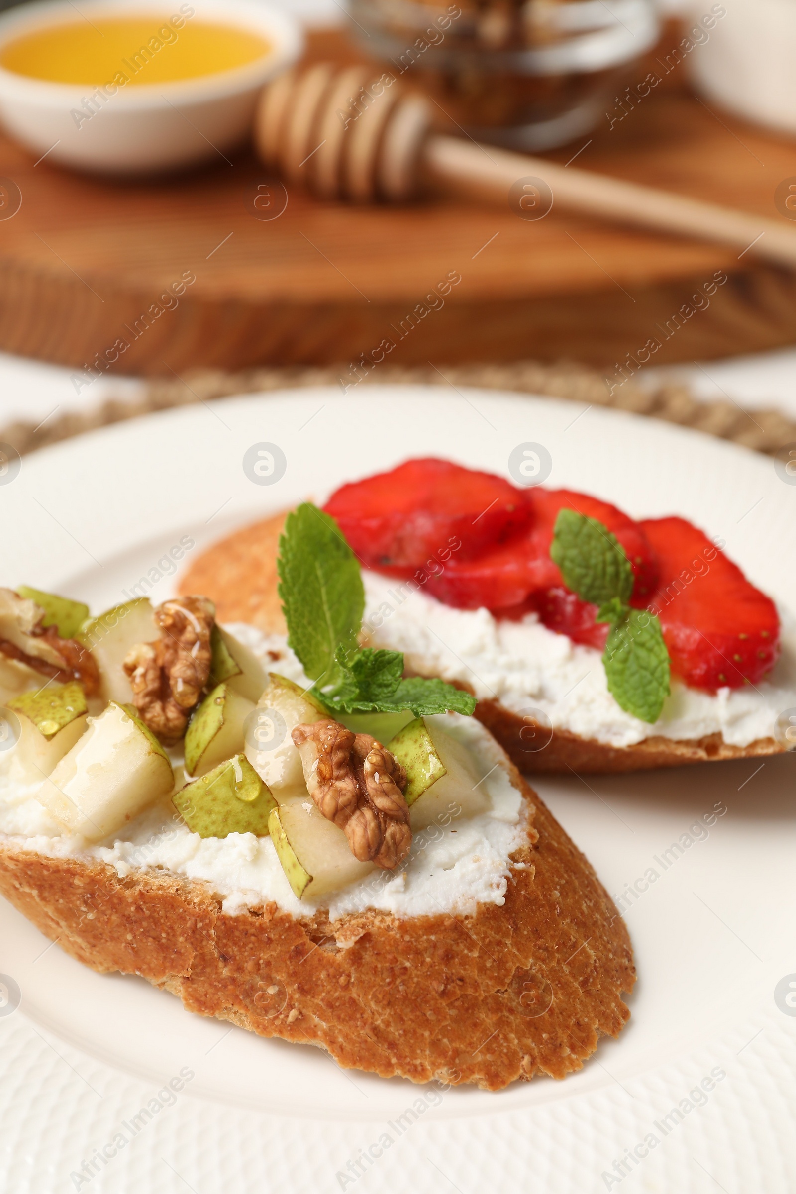 Photo of Delicious ricotta bruschettas with pear, strawberry and walnut on white table, closeup