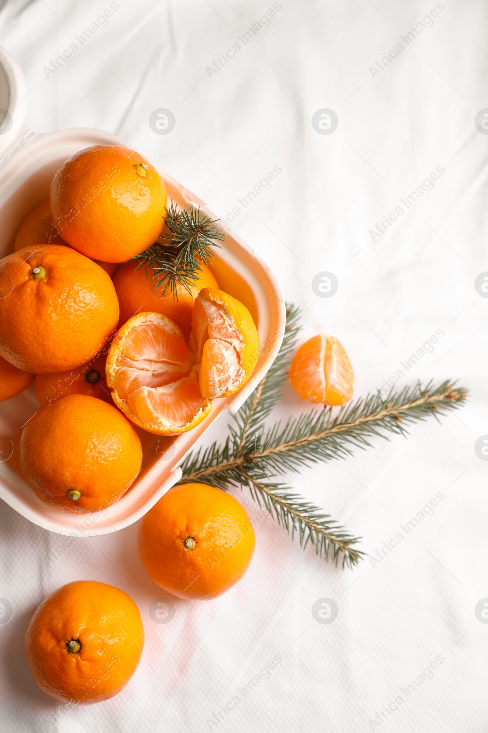Photo of Box with delicious ripe tangerines and fir branches on white bedsheet, flat lay