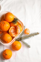 Box with delicious ripe tangerines and fir branches on white bedsheet, flat lay