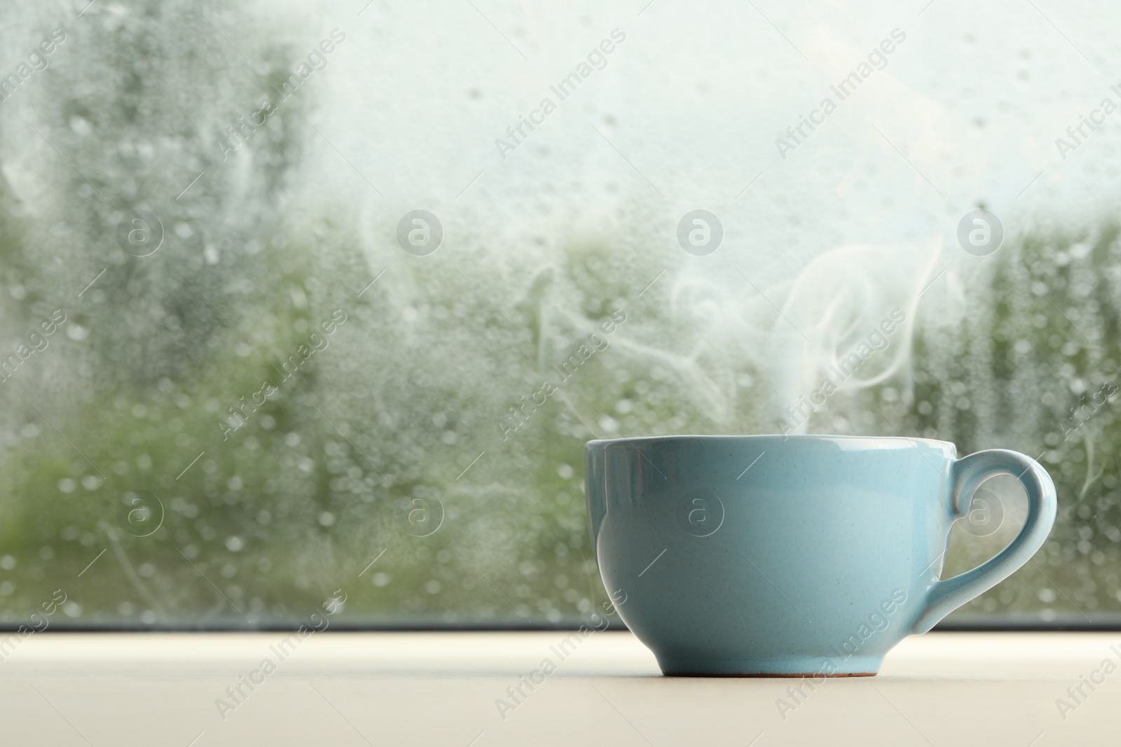 Photo of Cup of hot drink near window on rainy day. Space for text