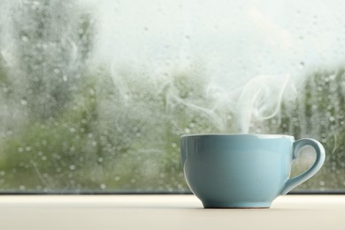 Cup of hot drink near window on rainy day. Space for text