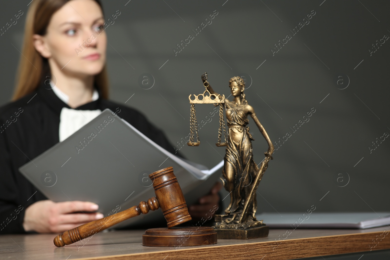 Photo of Judge with folder working in courtroom, selective focus. Mallet and figure of Lady Justice on wooden table
