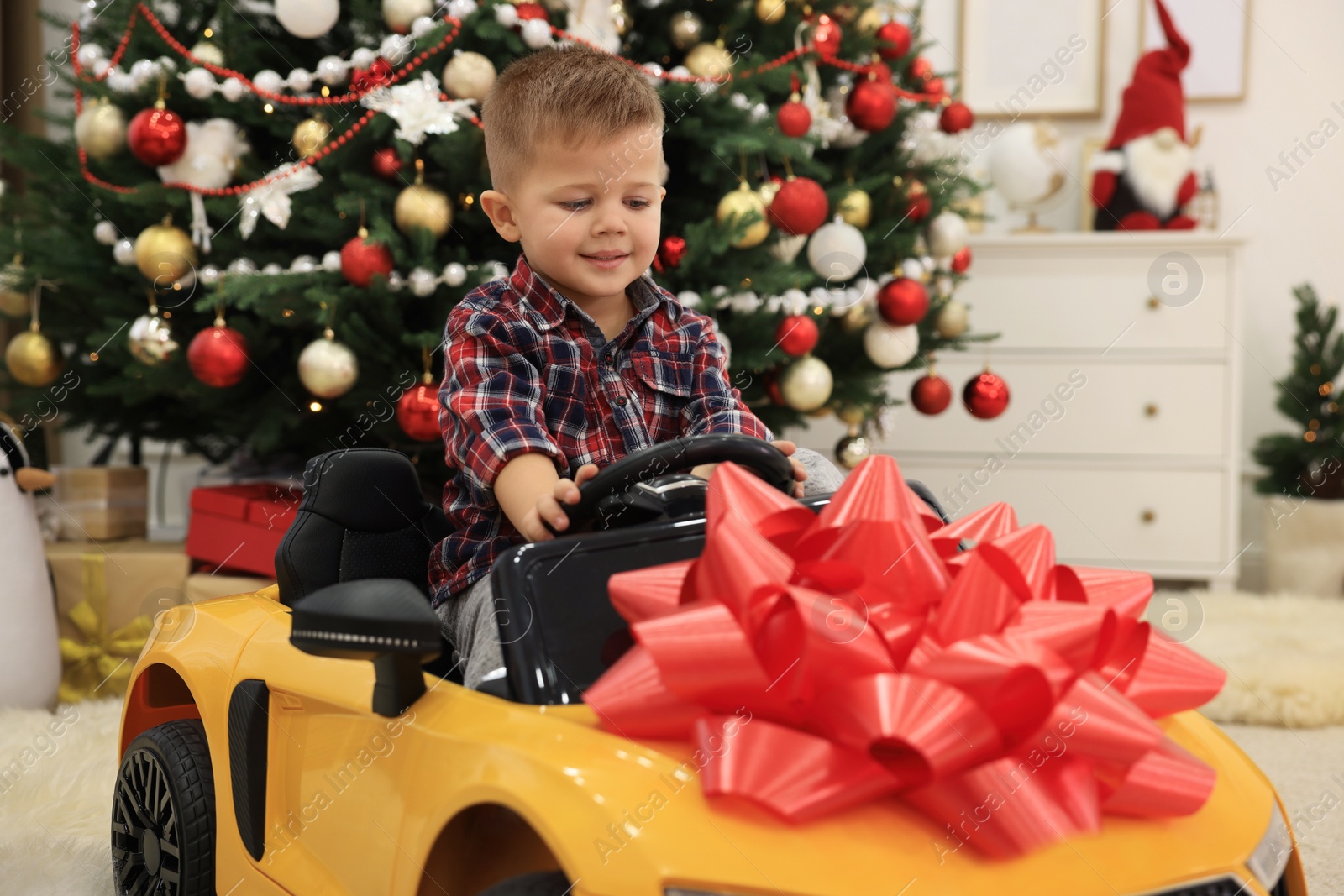 Photo of Cute little boy driving toy car in room decorated for Christmas