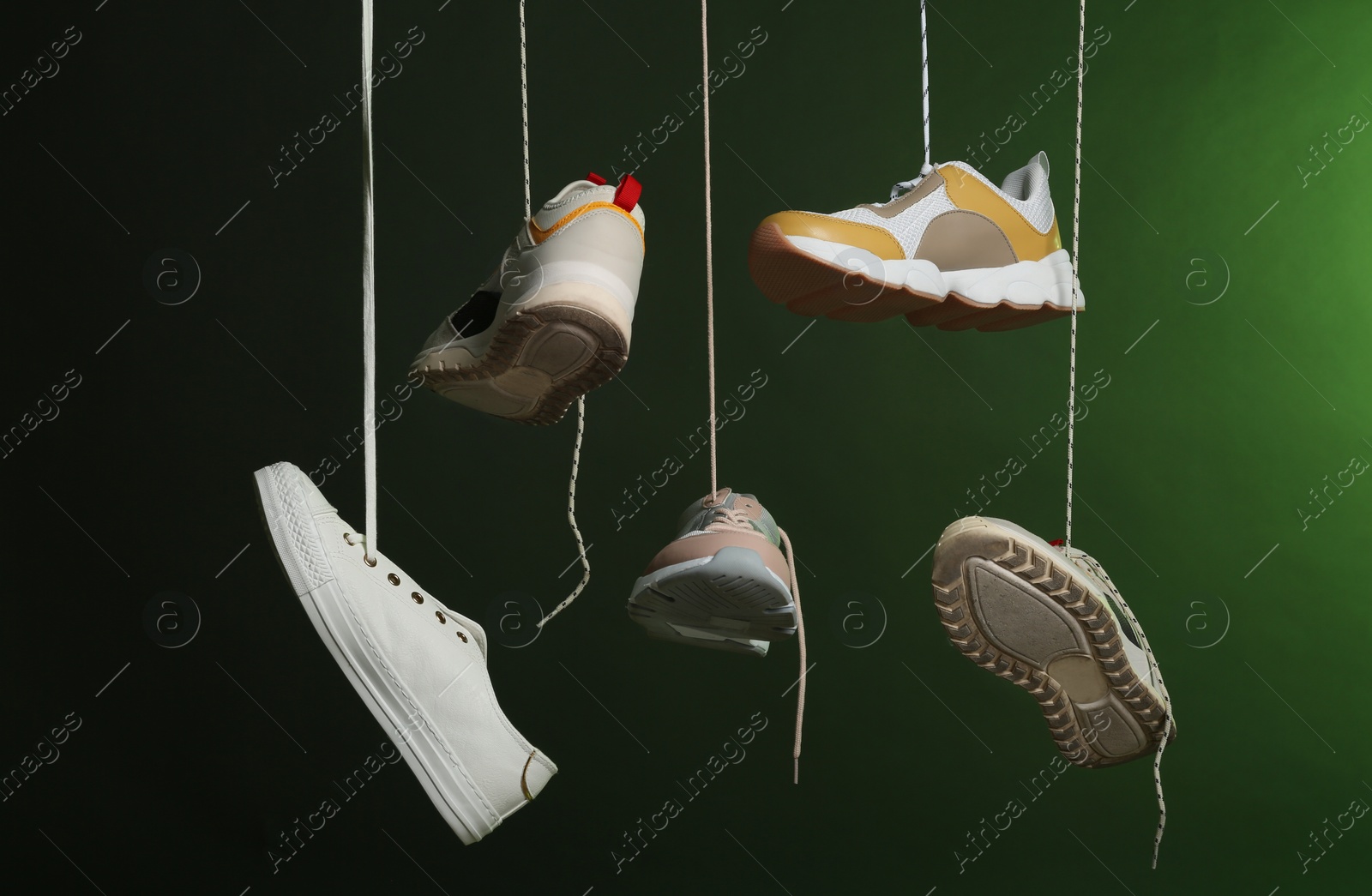 Photo of Different sneakers hanging on dark background. Stylish shoes