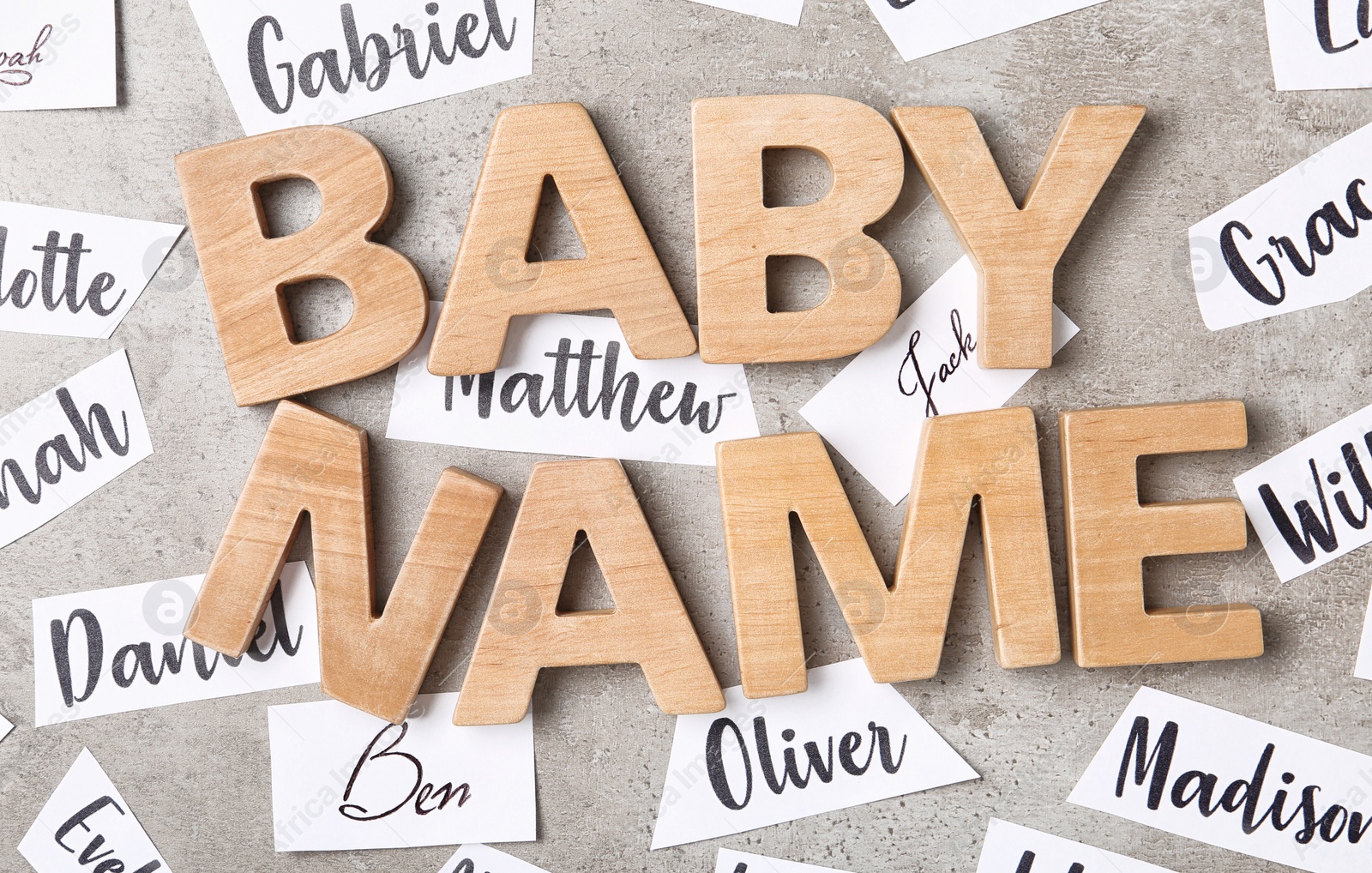 Photo of Paper sheets with different baby names and wooden letters on grey background, flat lay