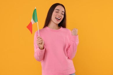 Emotional young woman holding flag of Italy on orange background