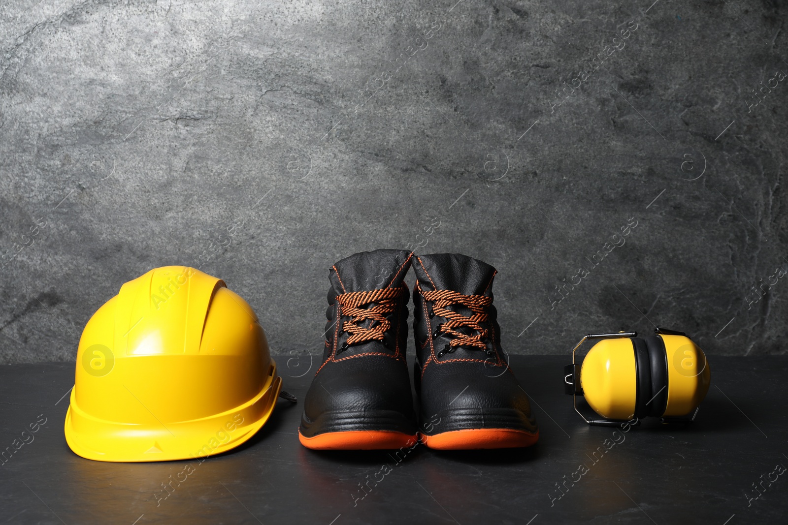 Photo of Hard hat, pair of working boots, and earmuffs on gray background, space for text