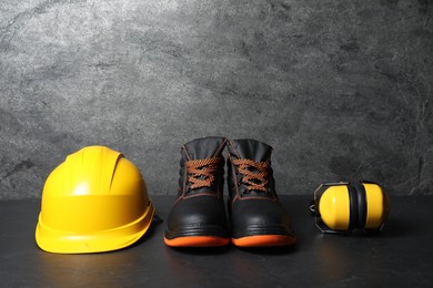 Photo of Hard hat, pair of working boots, and earmuffs on gray background, space for text