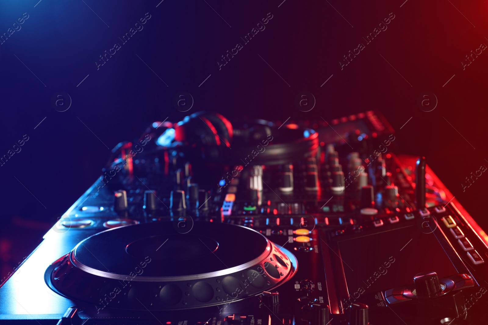 Photo of Closeup view of modern DJ controller with headphones on dark background