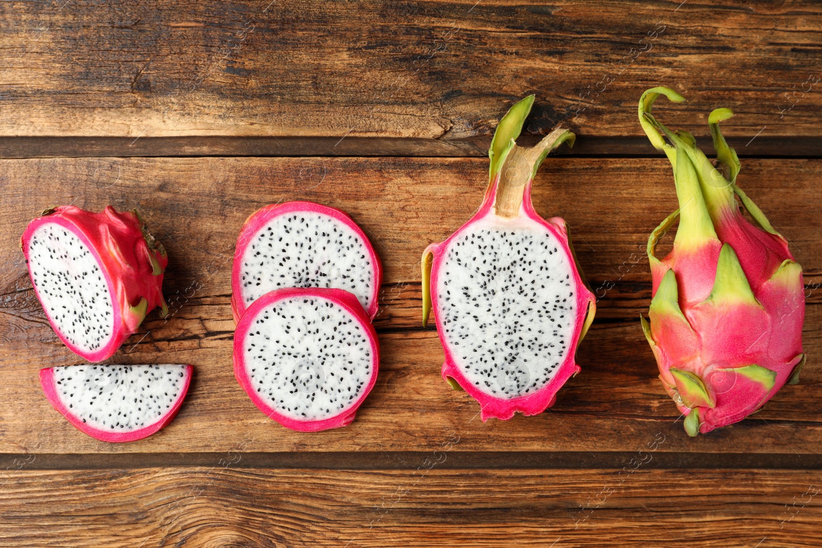 Photo of Delicious cut and whole dragon fruits (pitahaya) on wooden table, flat lay