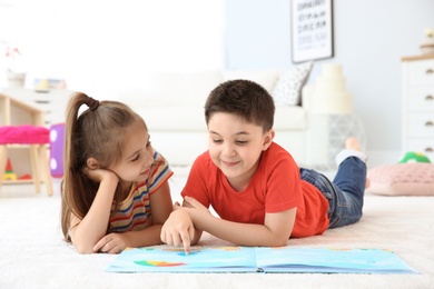 Photo of Cute little children reading book on floor in playing room