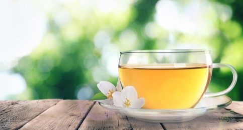 Image of Cup of jasmine tea and fresh flowers on wooden table outdoors, space for text. Banner design