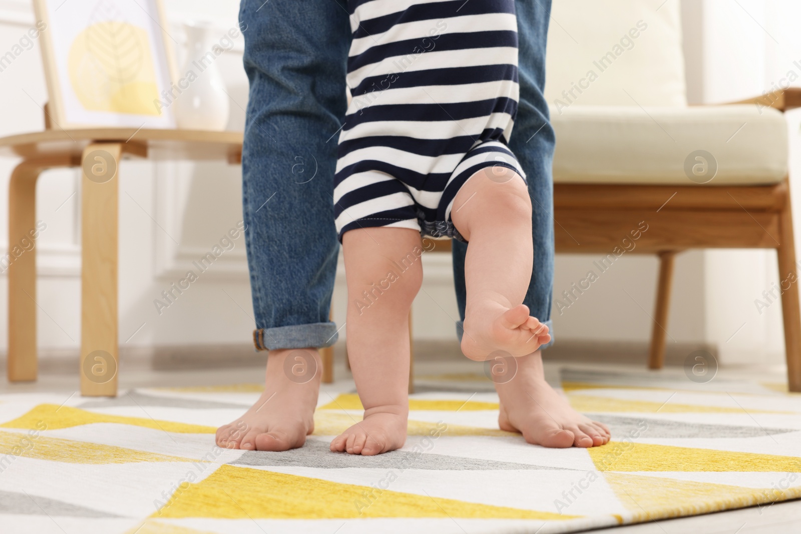 Photo of Mother supporting her baby son while he learning to walk on carpet at home, closeup