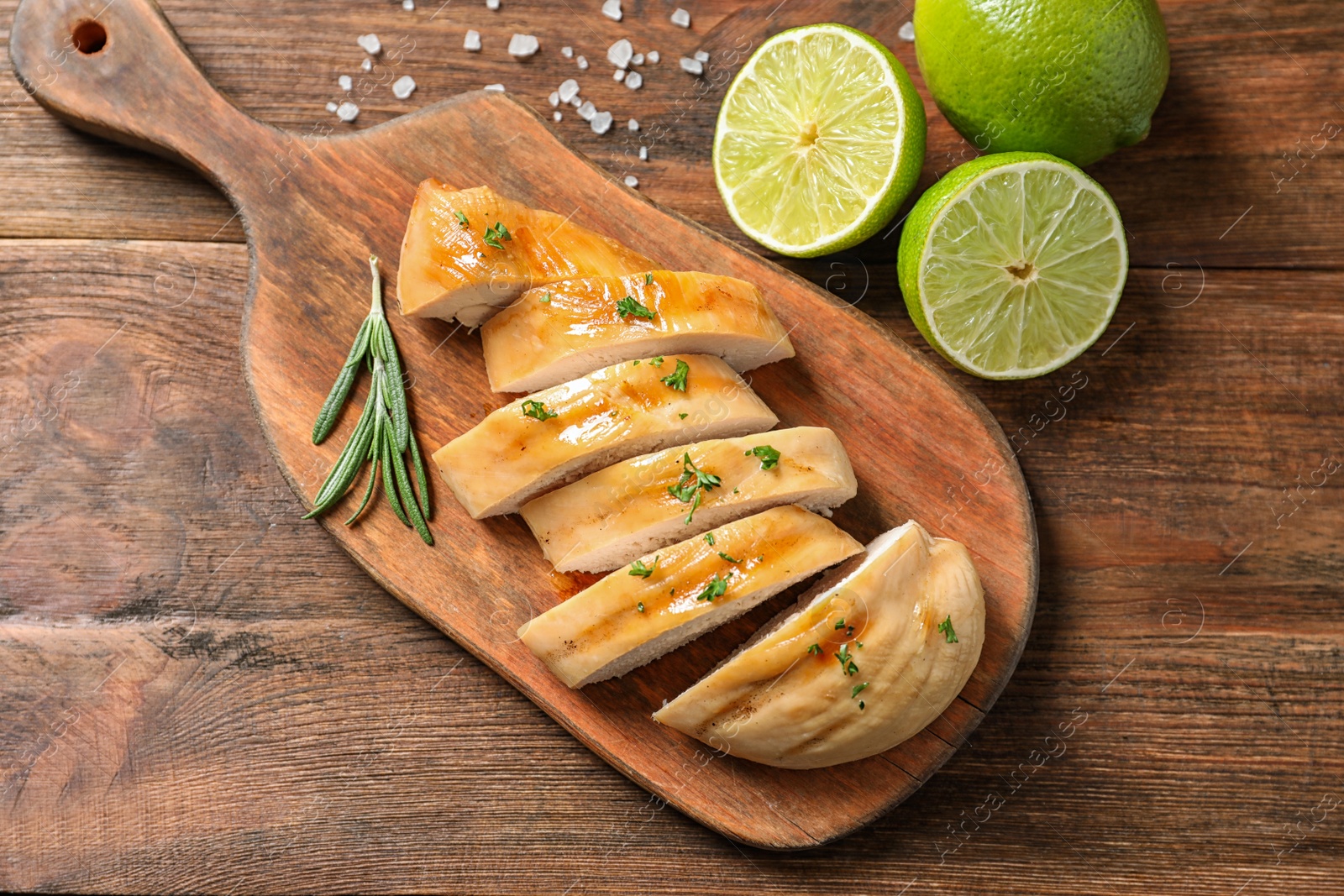 Photo of Board with fried chicken breast and limes on wooden background, top view