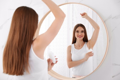 Beautiful young woman applying deodorant in bathroom