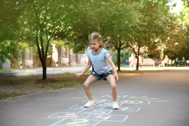 Photo of Little child playing hopscotch drawn with colorful chalk on asphalt