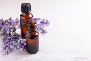 Photo of Bottles of essential oil and lavender flowers on white wooden background. Space for text