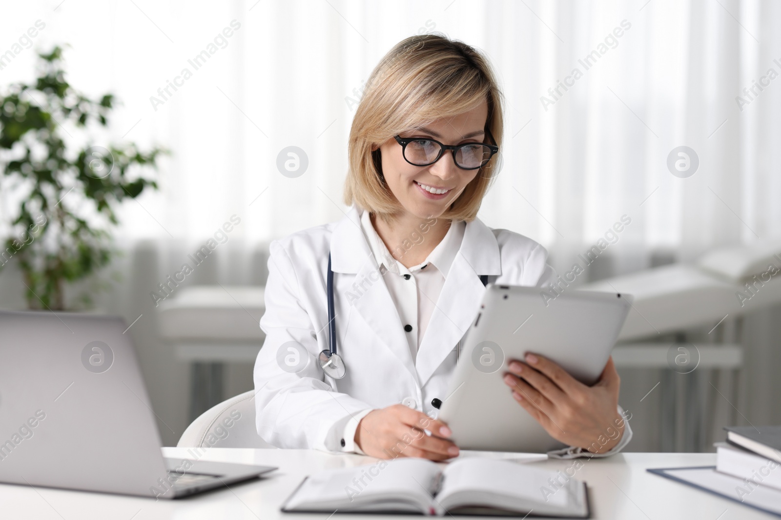 Photo of Smiling doctor with tablet having online consultation at table in office