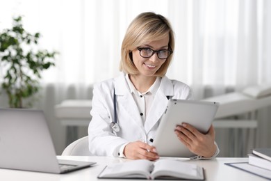 Smiling doctor with tablet having online consultation at table in office