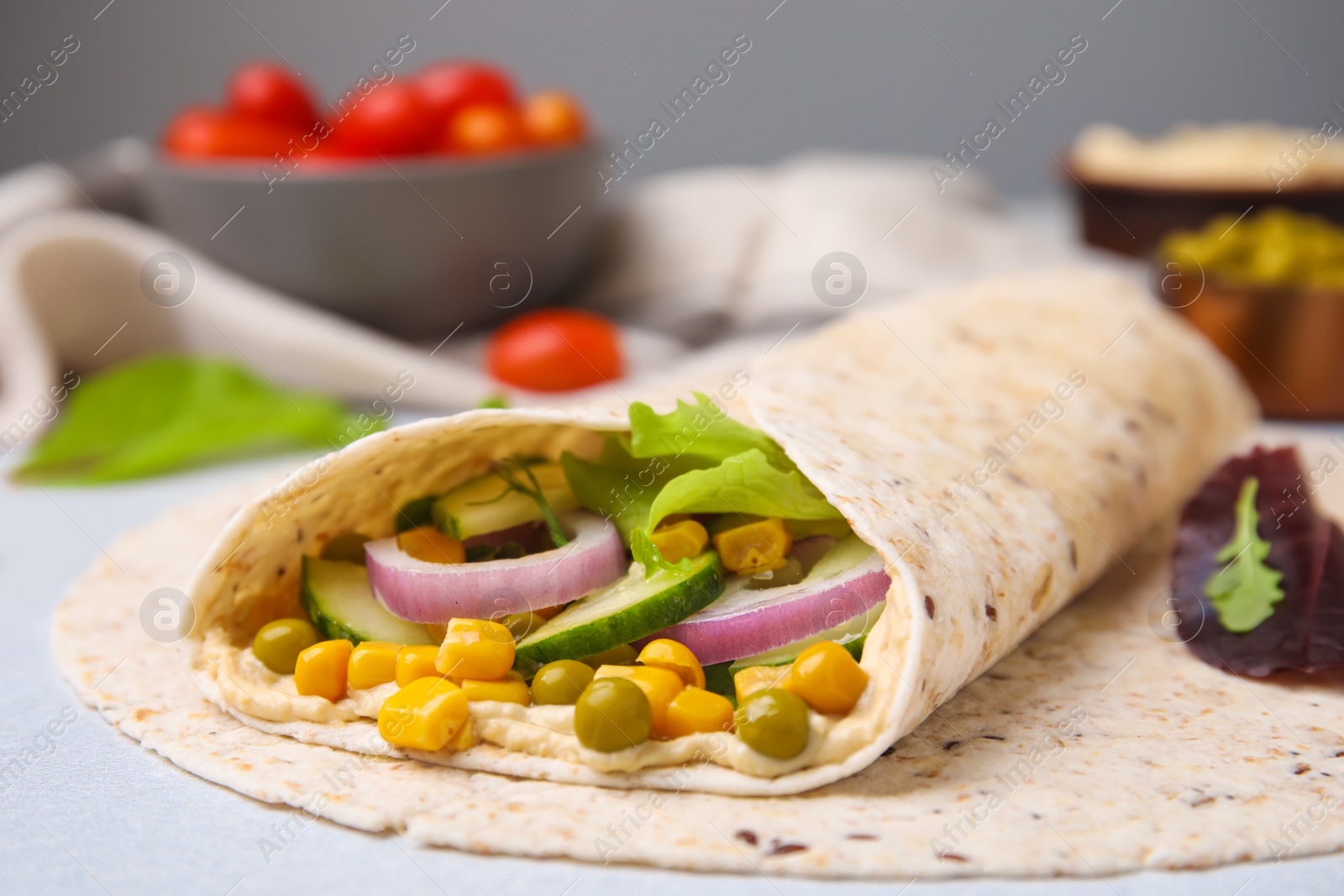 Photo of Delicious hummus wrap with vegetables on table, closeup