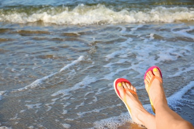 Photo of Closeup of woman with flip flops on sand near sea, space for text. Beach accessories