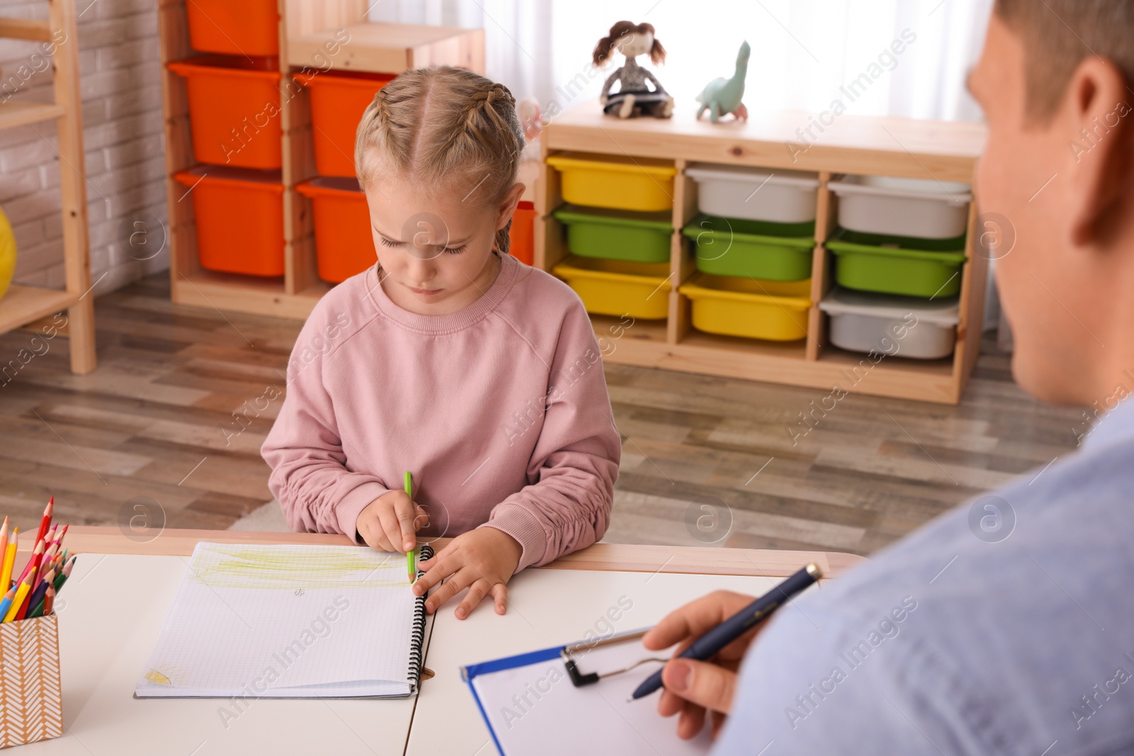 Photo of Little girl on appointment with child psychotherapist indoors