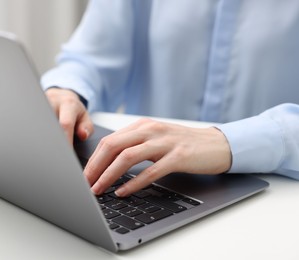 Photo of E-learning. Woman using laptop at white table indoors, closeup