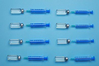 Photo of Disposable syringes with needles and vials on light blue background, flat lay