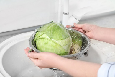Photo of Woman washing fresh cabbage in colander under water, closeup