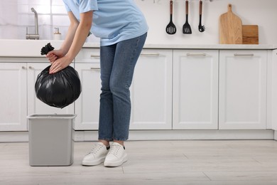 Photo of Woman taking garbage bag out of trash bin in kitchen, closeup. Space for text