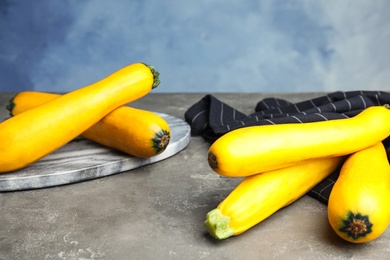 Photo of Fresh ripe yellow zucchinis on grey table against blue background, space for text