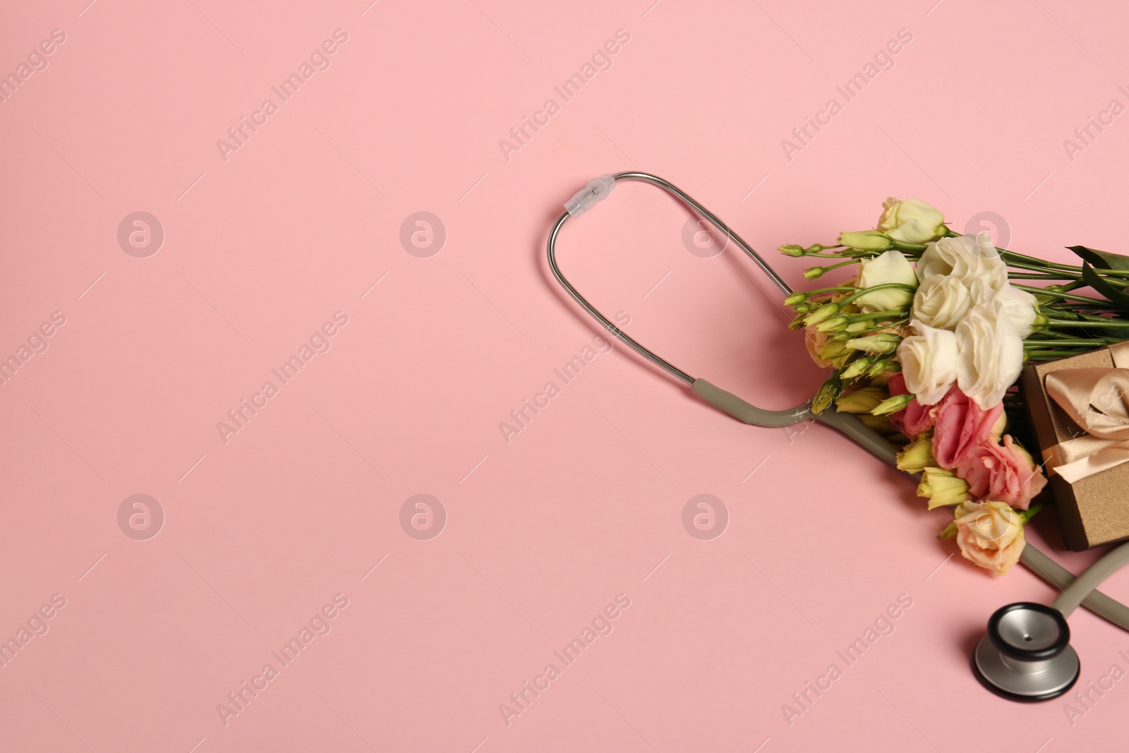 Photo of Stethoscope, gift box and eustoma flowers on pink background, space for text. Happy Doctor's Day