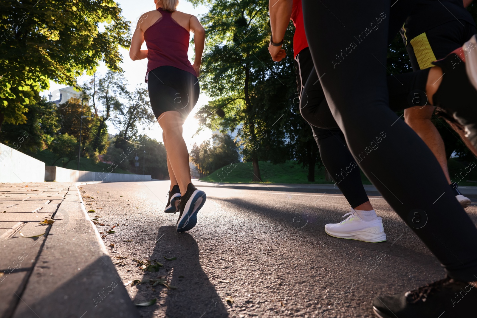 Photo of Group of people running outdoors on sunny day, back view