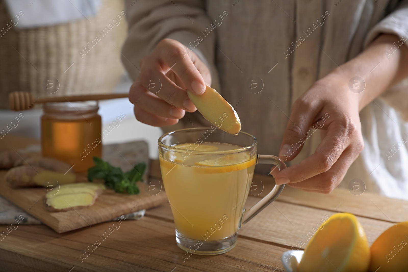 Photo of Woman making aromatic ginger tea at wooden table indoors, closeup