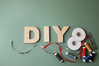 Photo of Abbreviation DIY made of wooden letters and sewing supplies on olive background, flat lay