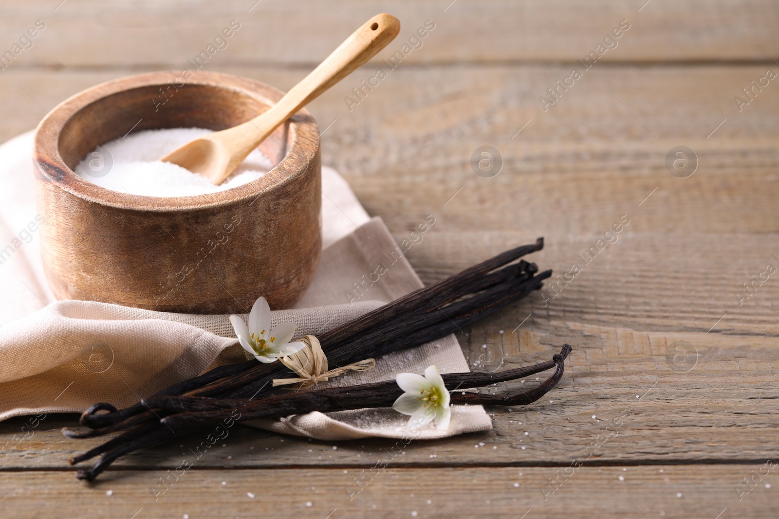 Photo of Vanilla pods, sugar in bowl and flowers on wooden table, closeup