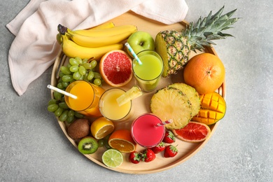 Wooden tray with glasses of different juices and fresh fruits on table, top view