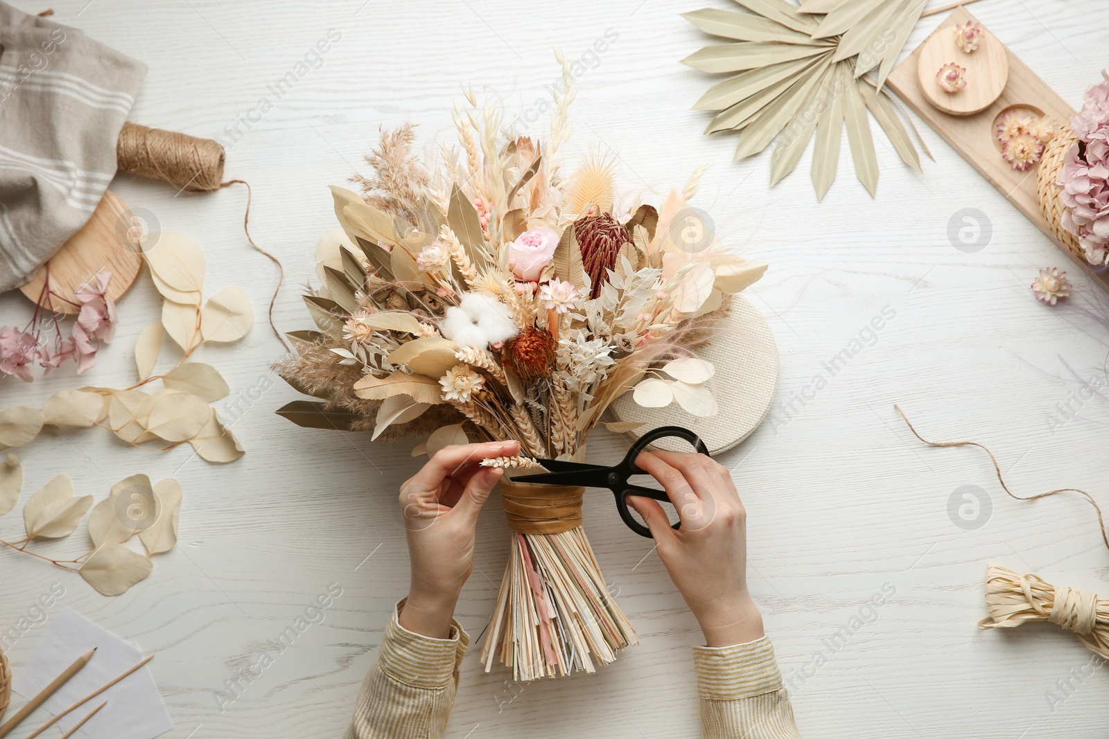 Photo of Florist making beautiful bouquet of dried flowers at white table, top view